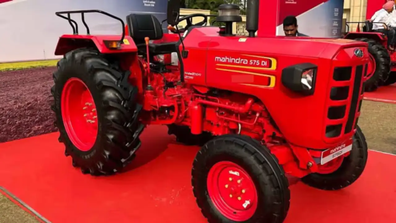 A new modern tractor driving through a green agricultural field in India during the monsoon season.